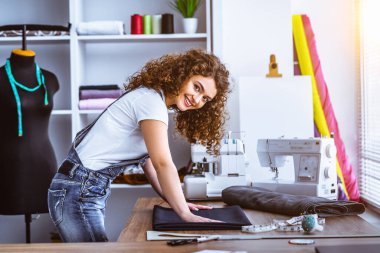 Gülümseyen kıvırcık kadın masaya dikiş atıyor.