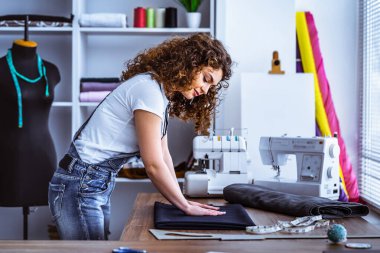 Kıvırcık kadın masaya dikiş dikiyor.