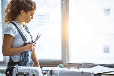 Elinde dikiş ekipmanıyla masanın yanında duran makaslı kadın.