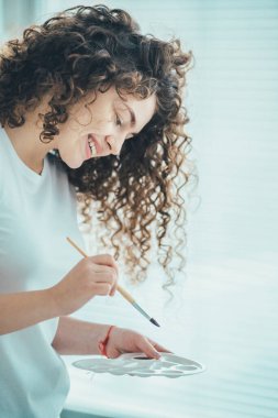 Fırçayla çalışan mutlu kıvırcık sanatçı.