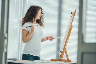 Mutlu kıvırcık ressam resim yapıyor sehpaya