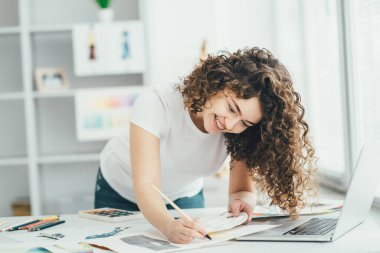 Masaya dizüstü bilgisayarla resim çizen kıvırcık kız.