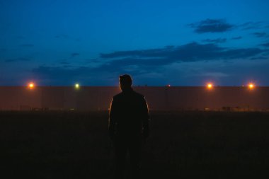 Adam binanın yanında duruyor. Akşam vakti.