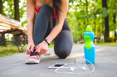 Kadın telefon ve şişenin yanındaki ayakkabıları bağlıyor.