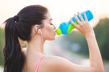 Sporcu kadın köprüde su içiyor.