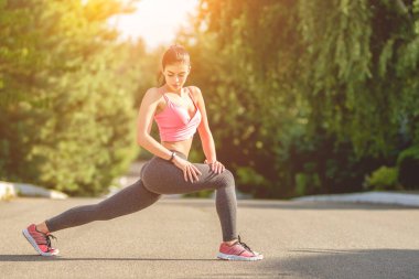 Sporcu kadın güneşli arka planda egzersiz yapıyor.