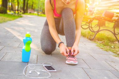 Sporcu kadın parkta ayakkabılarını bağlıyor.