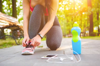 Sporcu kadın parkta ayakkabılarını bağlıyor.