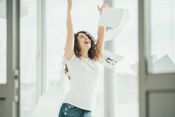 The happy woman throwing papers near the window