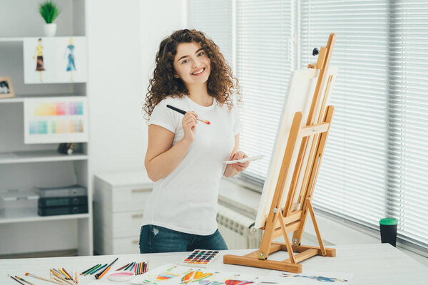 The cute woman with an art brush painting a picture on the easel