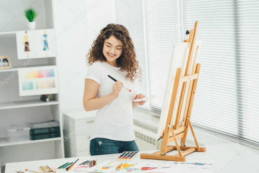 The cute woman with an art brush painting a picture on the easel