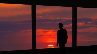 Güzel günbatımı arka planında panoramik pencerenin yanında duran adam.
