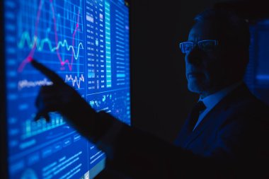 Büyük mavi ekranda grafiklerle çalışan eski iş adamı.