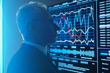 İş adamı büyük siyah ekranın yanında grafiklerle duruyor.