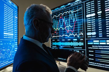 İş adamı karanlık odadaki büyük dijital ekranın yanında duruyor.