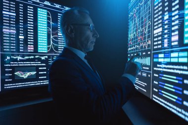 İş adamı karanlık odadaki büyük dijital ekranın yanında duruyor.