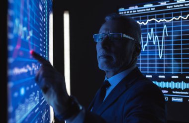 Büyük mavi ekranda grafiklerle çalışan eski iş adamı.