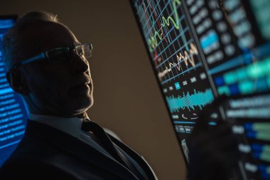 Yaşlı işadamı karanlık odadaki büyük dijital ekranda çalışıyor.