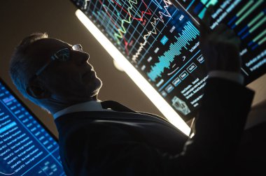 Yaşlı işadamı karanlık odadaki büyük dijital ekranda çalışıyor.