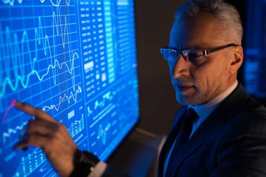 Büyük mavi ekranda grafiklerle çalışan eski iş adamı.