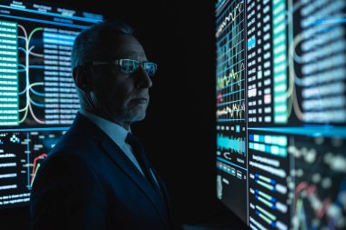 İş adamı karanlık odada büyük ekranın yanında duruyor.