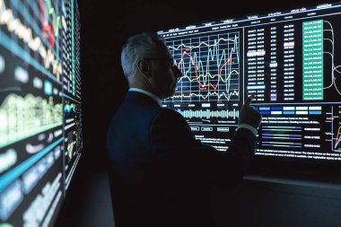 İş adamı karanlık odadaki büyük dijital ekranın yanında duruyor.