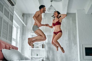 Yatakta zıplayan iç çamaşırlı seksi adam ve kadın.