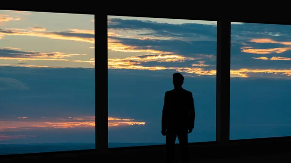 The businessman standing near the panoramic window on the  sunset background
