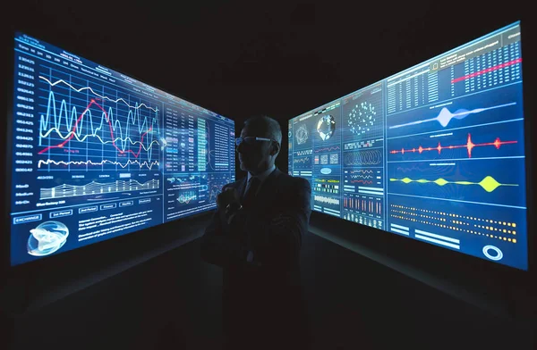 Büyük mavi ekranın yanında grafiklerle duran yaşlı işadamı.