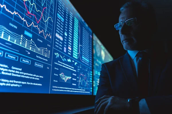Büyük mavi ekranın yanında grafiklerle duran yaşlı işadamı.