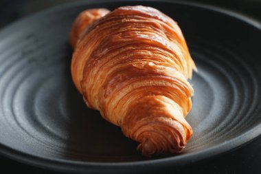 Classic French butter croissant on a Japanese ceramic black plate. Micro dark food photography clipart