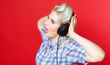 Kırmızı arka planda duran kulaklıklı güzel bir sarışın.