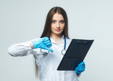 Covid19, koronavirüs, bir sağlık ve doktor konsepti. Kadın bir doktorun portresi, kötü sonucun baş parmak aşağı olduğunu gösteriyor. Virüs bulaşmasını önlemek için tıbbi maske takıyor. Beyaz önlük.