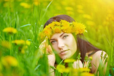 Güzel kız kafasında karahindiba çelengiyle baharın tadını çıkarıyor.