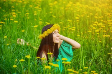 Güzel kız kafasında karahindiba çelengiyle baharın tadını çıkarıyor.