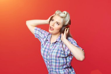 Kırmızı arka planda duran kulaklıklı güzel bir sarışın.