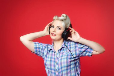 Kırmızı arka planda duran kulaklıklı güzel bir sarışın.