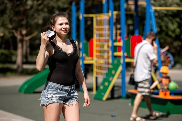 girl in the background of the playground takes off a medical mask.