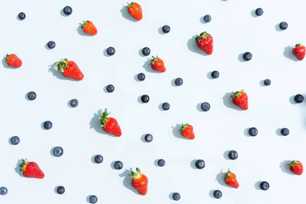 Fruit pattern of blueberries and strawberries. Blue background flatlay