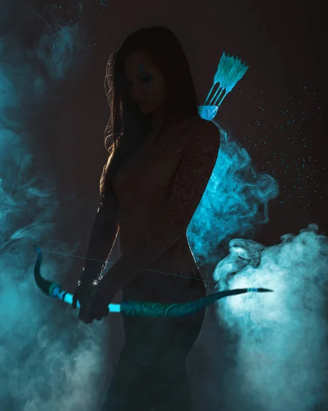 Young woman with a glowing bow and arrow on a dark background