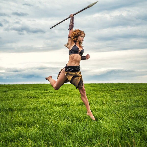 Girl warrior in the field. Jump with a spear.