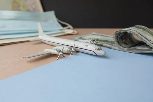 a toy plane on the background of dollar bills, a map and a face mask, the concept of closing borders around the world due to coronavirus, financial losses of airlines and tour operators.