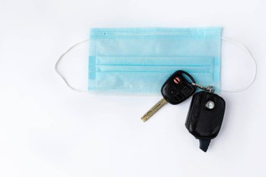 Araba anahtarları ve tıbbi maske beyaz bir arka planda. Koronavirüs salgını yüzünden karantina sona erdi. Düz yatıyordu.