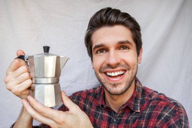 Portrait of a young cheerful guy with a happy smile while holding a shiny moka pot with a coffee in a shirt clipart