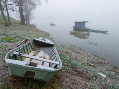 Eski balıkçı kıyafeti ıssız ve sessiz siste terk edilmiş görünüyor. Suyun içinden çıkartılan eski bir balıkçı teknesi ve kıyıya demirlenmiş yüzen balıkçı kulübesi sislerin içinde kaybolur ve bulanıklaşır..