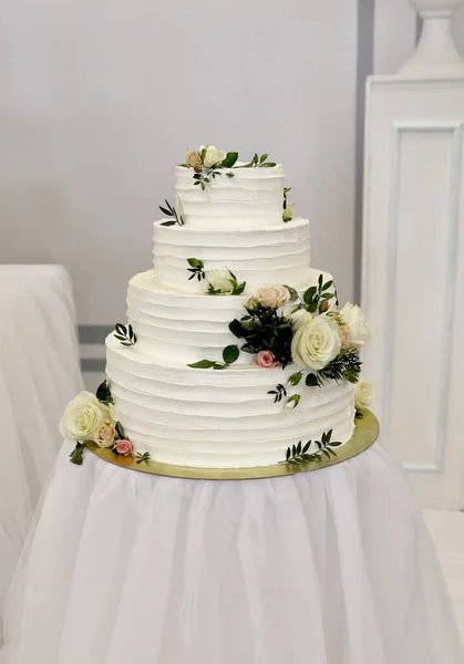 大きな白い丸いケーキ4層の高さ新鮮な花で飾られた結婚式白い背景に白い丸いテーブルの上に立つ緑の葉 — ストック写真