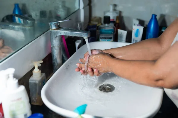 Female adult washing hands and arms properly with soap under the sink / wash basin in the washroom to battle Coronavirus. Bathroom console, hand wash with lot of products in the backdrop, space to add text