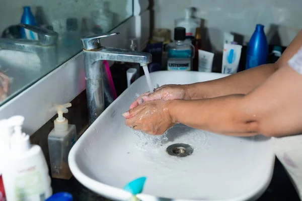 Yetişkin bir kadın, Coronavirus 'la savaşmak için lavabonun ve lavabonun altındaki sabunla ellerini ve kollarını düzgün bir şekilde yıkıyor. Banyo konsolu, arka planda bir sürü ürünle el yıkama, metin eklemek için yer