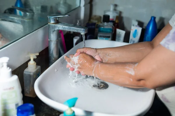 Yetişkin bir kadın, Coronavirus 'la savaşmak için lavabonun ve lavabonun altındaki sabunla ellerini ve kollarını düzgün bir şekilde yıkıyor. Banyo konsolu, arka planda bir sürü ürünle el yıkama, metin eklemek için yer