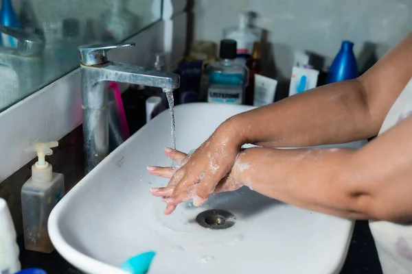 Yetişkin bir kadın, Coronavirus 'la savaşmak için lavabonun ve lavabonun altındaki sabunla ellerini ve kollarını düzgün bir şekilde yıkıyor. Banyo konsolu, arka planda bir sürü ürünle el yıkama, metin eklemek için yer